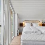 Schlafzimmer mit Doppelbett, Holzdecke und großem Fenster zur Terrasse.