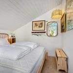 Schlafzimmer mit Doppelbett, Holzboden und Wandbildern. Decke mit weißen Holzdielen.