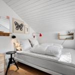 Schlafzimmer mit Bett, Wandregalen und Fenster unter schrägem Dach.
