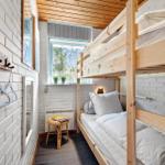 Zimmer mit Holz-Etagenbett, weißer Ziegelwand und Fenster mit Pflanzen.