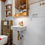 Badezimmer mit Toilette, Waschbecken und Spiegelschrank. Holzregale und goldfarbene Armaturen.
