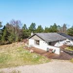 Ein Haus mit Holzterrasse und Garten, umgeben von Bäumen unter blauem Himmel.