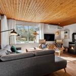 Wohnzimmer mit Holzdecke, Sofa, Kamin und großem Fenster. Essbereich mit Holztisch und Stühlen.