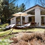Hängematten und Sonnenschirm im Garten vor einem weißen Haus mit Terrasse.