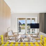 Wohnzimmer mit gelbem Sofa, Fernseher und Terrasse mit Blick.