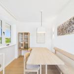 Esszimmer mit Holztisch, Bänken und Glasvitrine. Fenster mit Blick auf Grün.