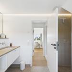 Badezimmer mit Dusche und Waschbecken. Blick in Wohnbereich mit Sitzgelegenheit.