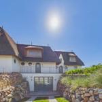 Haus mit Strohdach, Steinmauern und Balkon unter blauem Himmel.