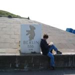 A person sits next to a sign reading Berlin 516 km.