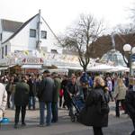 Many people move around a busy street with market stalls and a white building.