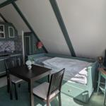 Bedroom with bed, table, chairs, and small kitchen under sloped ceiling.