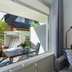Durchgehendes Fenster zeigt Garten mit Tisch und Stühlen. Sofa mit Kissen und Stehlampe im Raum.