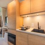 Küche mit Holzschränken, Spüle und Herd. Im Hintergrund ist ein Schrank und ein Stuhl sichtbar.