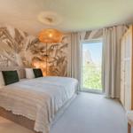 Schlafzimmer mit Bett, Wandtapete und Fenster. Holzgarderobe und Hängeschild.