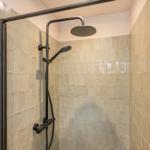Dusche mit Glaswand und schwarzen Armaturen an beigefarbenen Fliesen