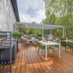 Terrasse mit Holzboden, weißem Pavillon, grünen Stühlen und Tischen, Pflanzen und Blick in den Wald.