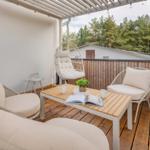 Terrasse mit Sitzgruppe, Tisch und Hängesessel. Holzdecke und Blick auf Wald.