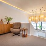 Ein Raum mit Sessel, Sideboard, Pflanzen und hängenden Lampen.