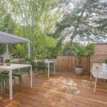 Terrasse mit Tisch, Stühlen und Pavillon. Holzdecke, Pflanzen und Bäume im Hintergrund.
