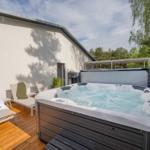 Außenbereich mit Whirlpool, Sonnenliegen und Holzterrasse neben einem Haus.