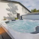 Ein Whirlpool mit blauem Wasser auf einer Holterrasse vor einem weißen Gebäude.
