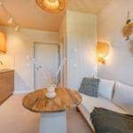 Wohnbereich mit Sofa, runden Tisch und Küchenzeile mit Holzmöbeln.