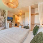Schlafzimmer mit Bett, Wandtapete und Blick in Wohnbereich mit Küchenzeile.