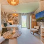 Schlafzimmer mit Bett, Sitzbank, Tisch und Fernseher. Wand mit Palmenmotiv.