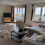 Living room with sofa, coffee table, and TV. Large windows with view of rooftops.