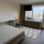 Room with double bed, desk, and balcony view of city
