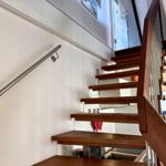 Holztreppe mit Metallgeländer führt zur oberen Etage. Weiße Wände und modernes Design.