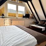 Schlafzimmer mit Dachschräge, Bett, Sofa und Fenster mit Jalousien.