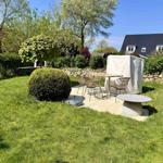 Garten mit Sitzgruppe, Tisch und Grill, umgeben von Gras und Sträuchern.