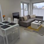 Wohn- und Essbereich mit Sofa, Tisch und Stühlen. Große Fenster mit Jalousien.