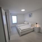 Schlafzimmer mit weißem Bett, Nachttischen und Fenster.