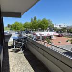 Terrasse mit Tisch und Stühlen. Blick auf Parkplatz und Geschäfte.