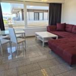 Wohn- und Essbereich mit rotem Sofa, weißem Tisch und großem Fenster mit Blick.