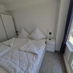 Schlafzimmer mit weißem Bett, Nachttischen und Fensterblick auf Garten.