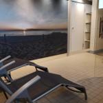 Liegemöbel vor einer Wand mit Strandmotiv, daneben Dusche und Schrank.