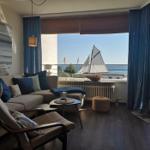 Wohnzimmer mit Meerblick, Sofa, Sessel und Segelschiffmodell auf Balkon.