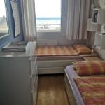 Zimmer mit zwei Betten, Fenster zum Meer und Schrank. Holzboden und Wandregale.