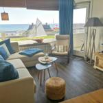 Wohnzimmer mit Sofa, Sessel und Fernseher. Blick auf Meer und Segelboot.