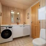 Bathroom with washing machine, toilet, and shower. Wooden walls and tiled floor.