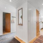 House with white walls, wooden doors, and kitchen area. Hanging plants and rugs are visible.