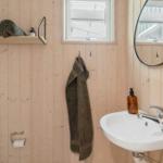 Bathroom with wooden walls, sink, mirror, and towel hooks.