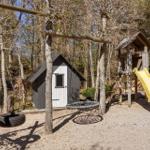 Play area with swing, slide, and playhouse in the woods.