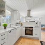 Kitchen with white cabinets, stainless steel oven, and wooden floor. View into the living room.