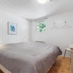 Bedroom with bed, window, coat hooks, and dresser. Walls paneled white, wooden floor.