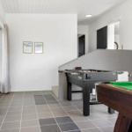 Room with pool table and foosball table, gray tiled floor and windows with curtains.