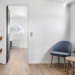 Entrance area with chair and table. Corridor to bedroom with arched window.